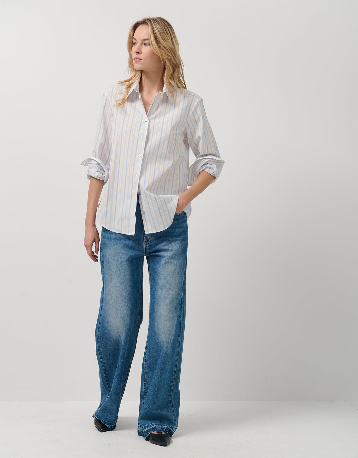 Woman wearing a white striped shirt and blue jeans on a plain background
