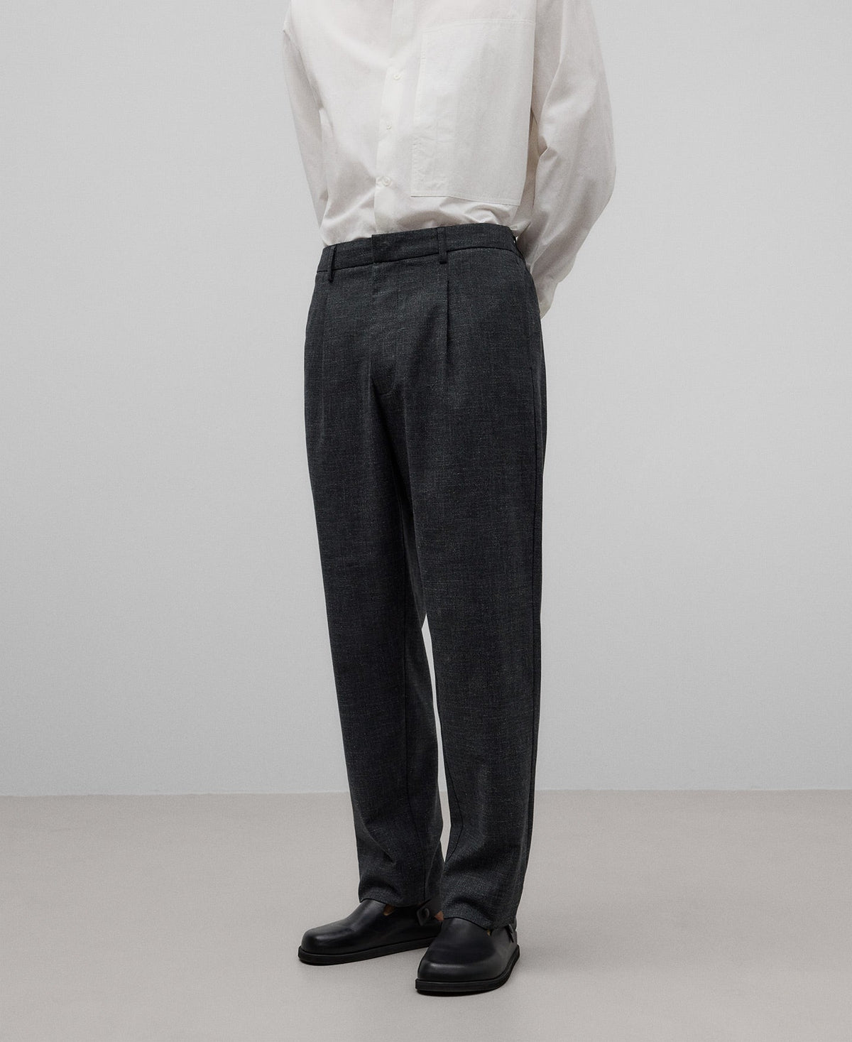 A man wearing gray melange relaxed fit trousers with a white shirt, standing against a neutral background.