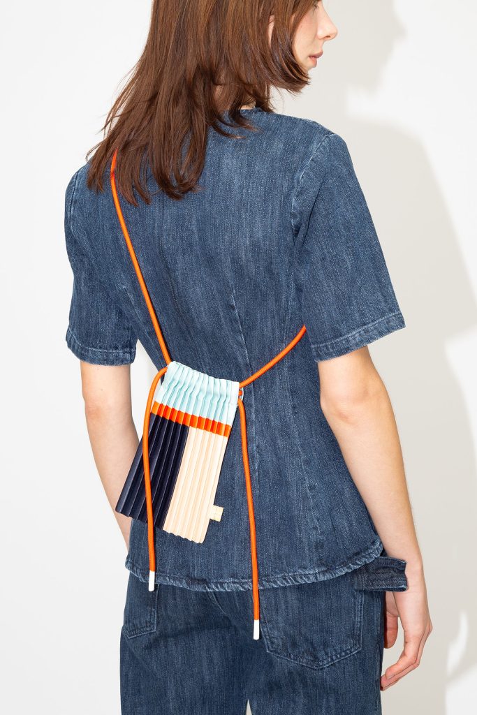 Person wearing a denim outfit with a colorful striped bag over one shoulder on a white background