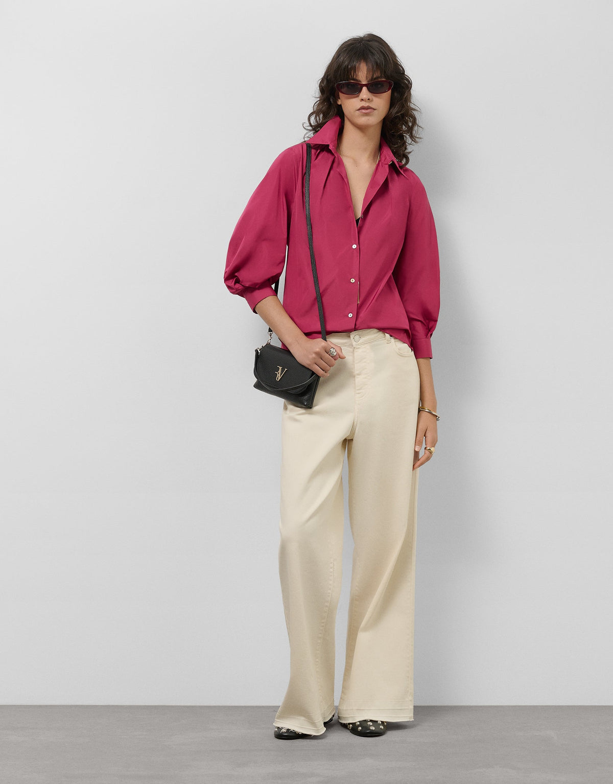 Woman wearing a pink blouse and beige pants with a black handbag against a white background