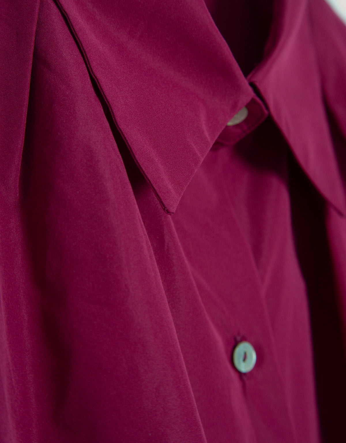 Close-up of a magenta shirt with a button on a neutral background