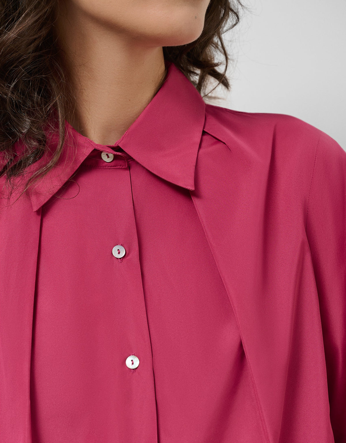 Close-up of a person wearing a pink shirt with a neutral background