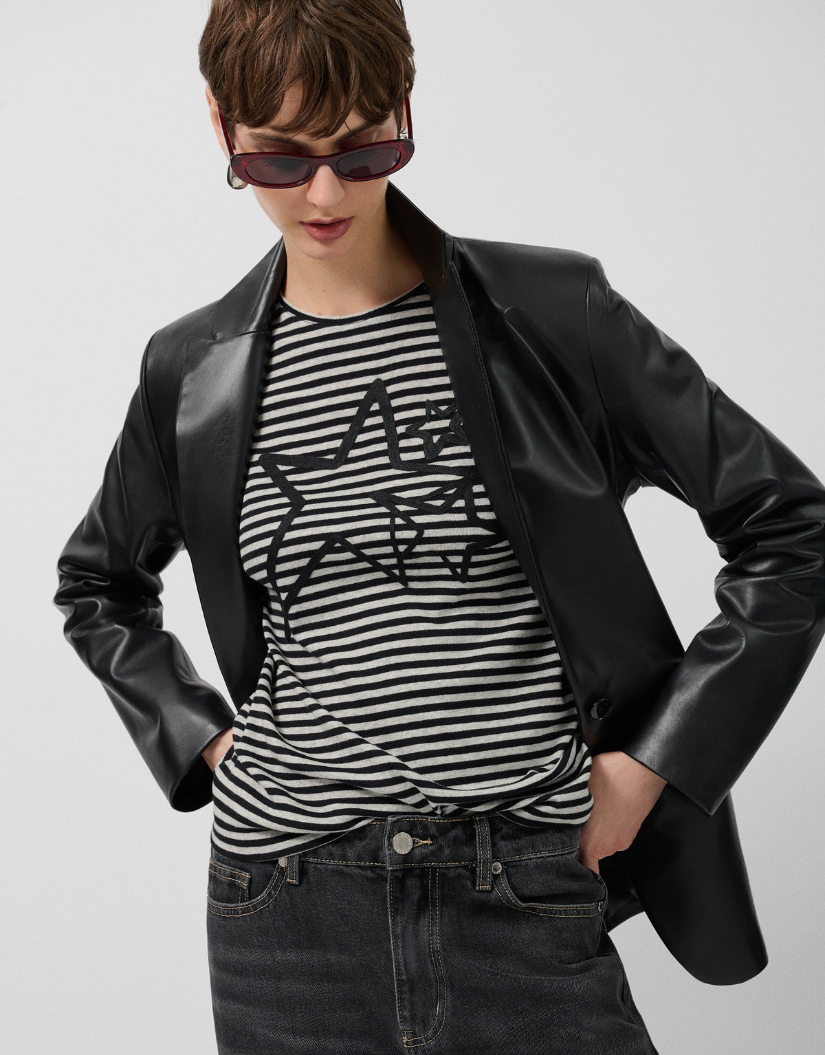 Person wearing a black leather jacket, striped shirt, and sunglasses on a plain background