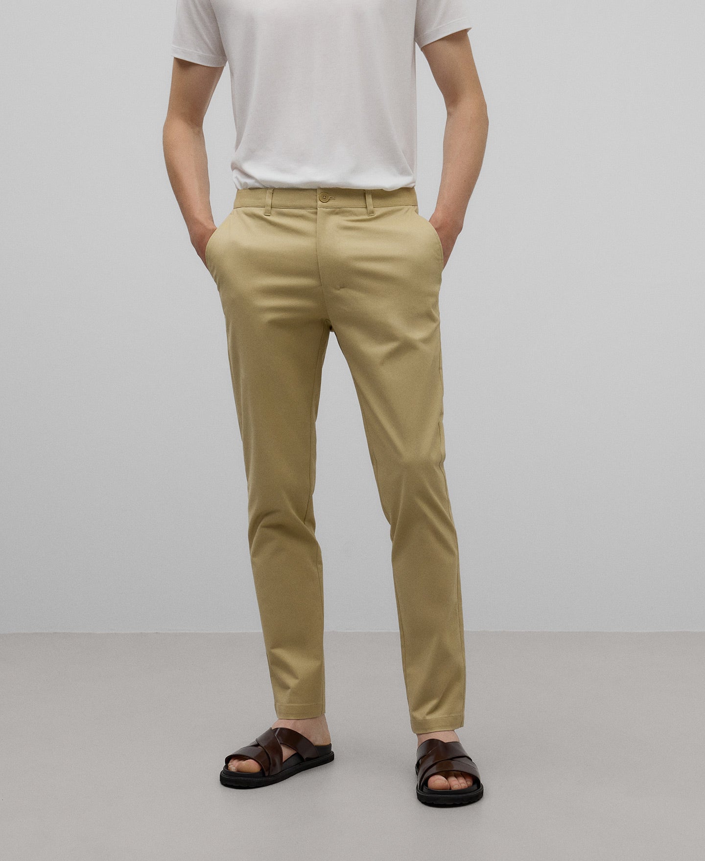 A man wearing slim fit cotton chino trousers in camel color with a white t-shirt, standing against a plain background.