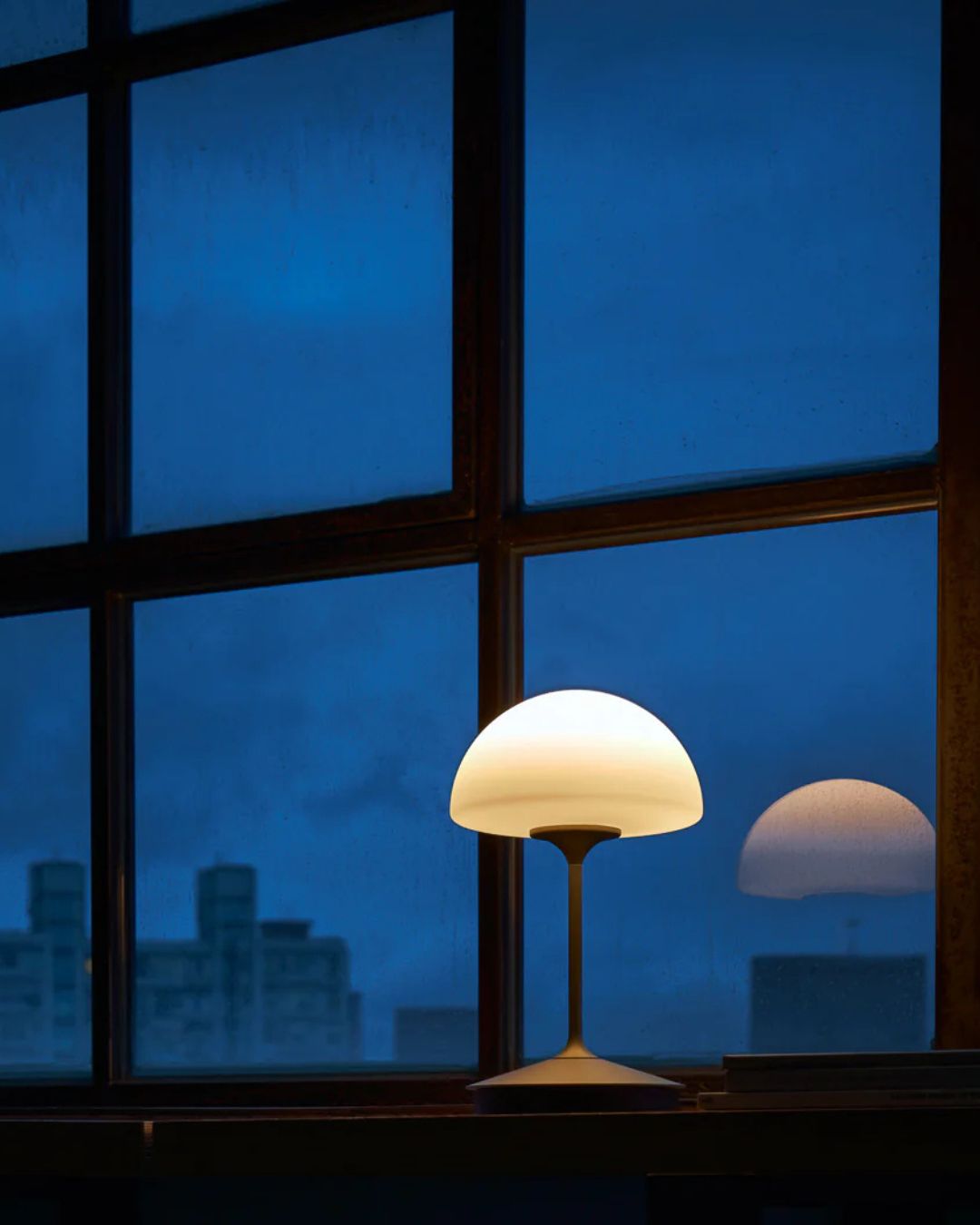 Lamp on a windowsill with a cityscape view at night