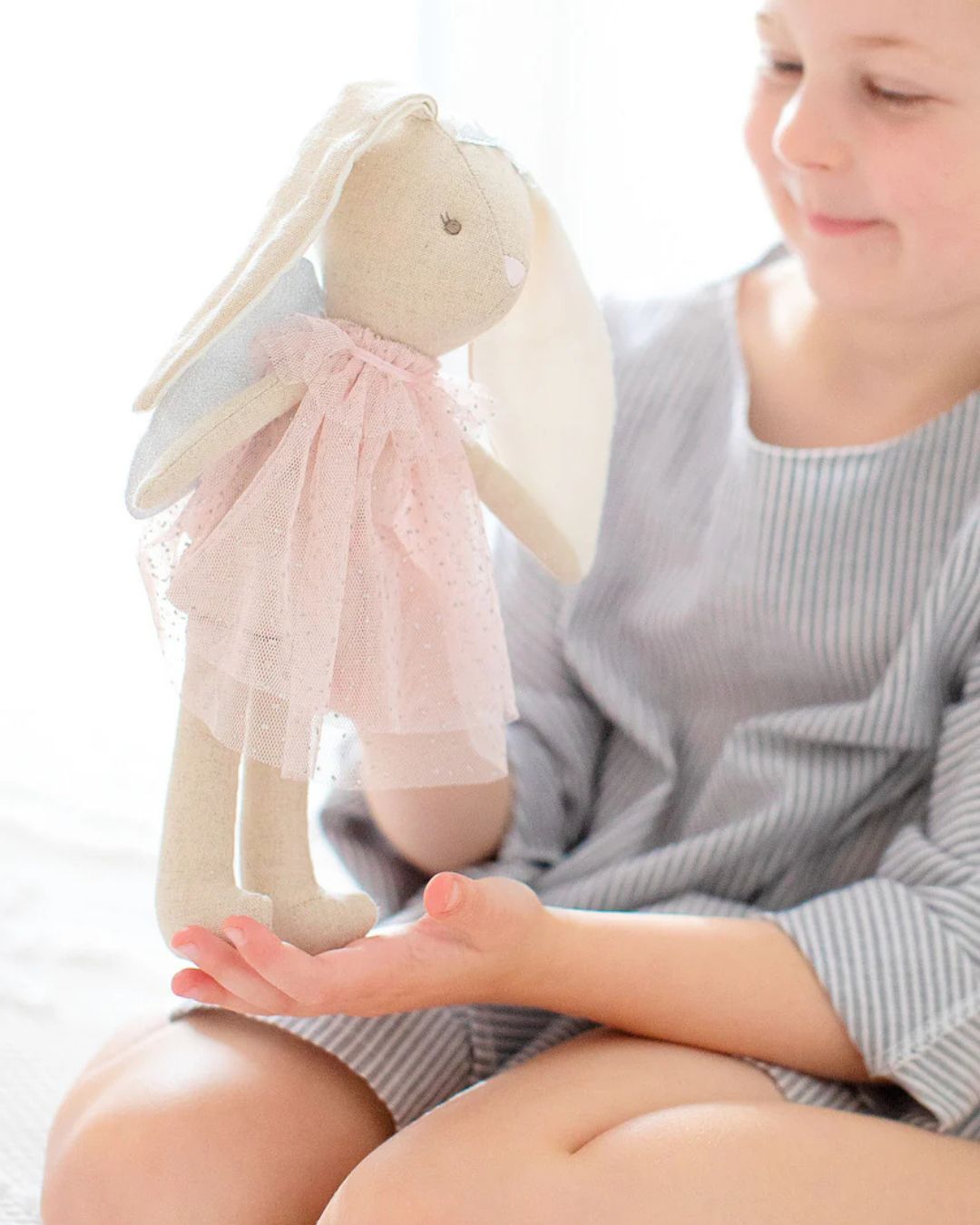 Child holding a plush bunny toy with a pink bow on a white background