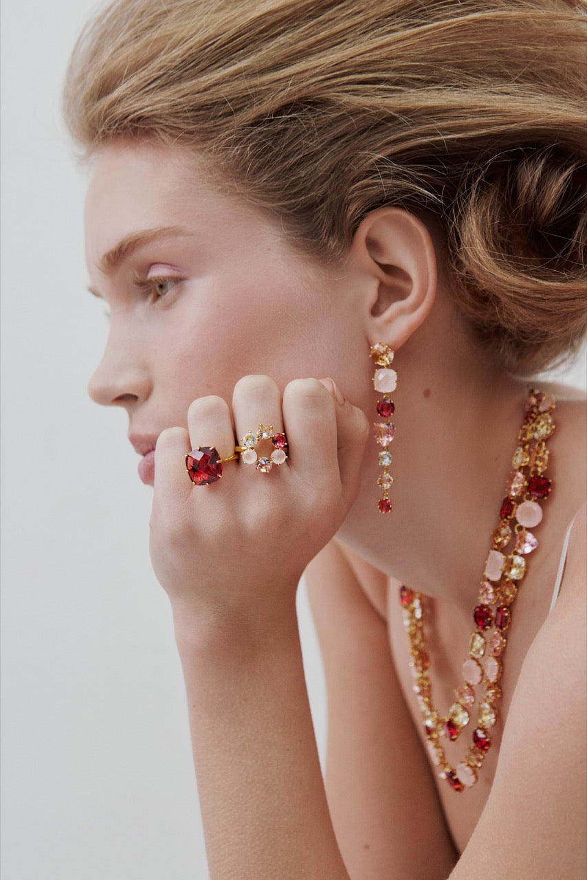 Woman wearing gold earrings, rings, and a necklace with red and gold stones on a white background