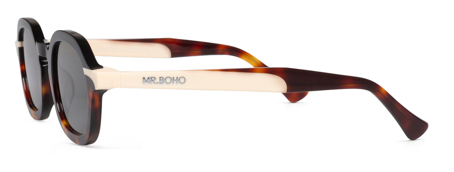 A pair of black and tortoiseshell framed oval sunglasses with dark lenses.  -side view mr boho logo on arm