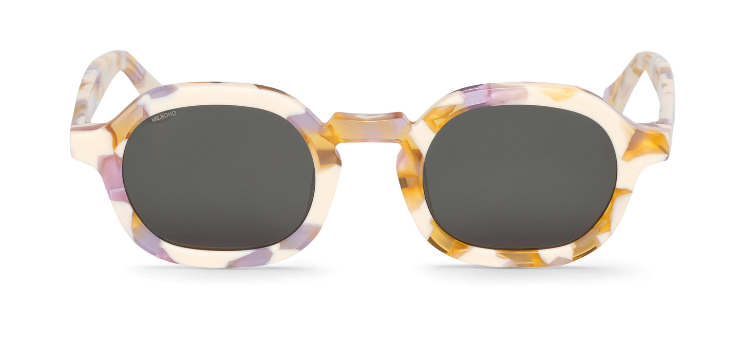 A pair of lilac/white mosiac pattern framed oval sunglasses with dark lenses.