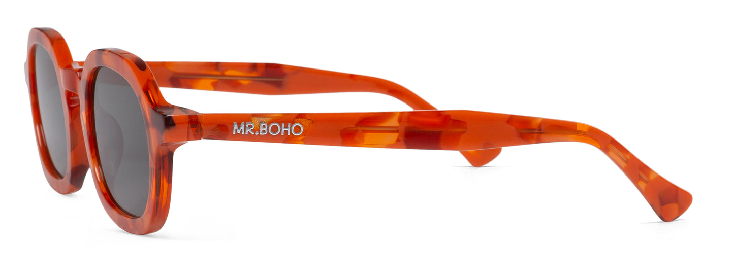A pair of orange mosaic pattern-framed oval sunglasses with dark lenses. - side view mr boho logo on arm