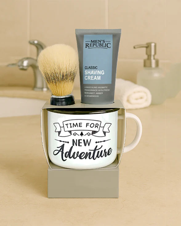Mug with 'Time for New Adventure' text, shaving cream, and brush on a bathroom counter.