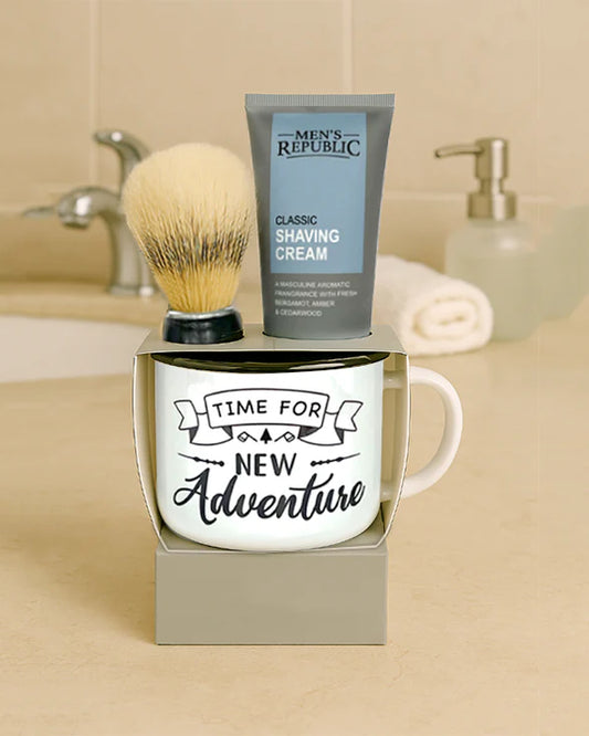 Mug with 'Time for New Adventure' text, shaving cream, and brush on a bathroom counter.
