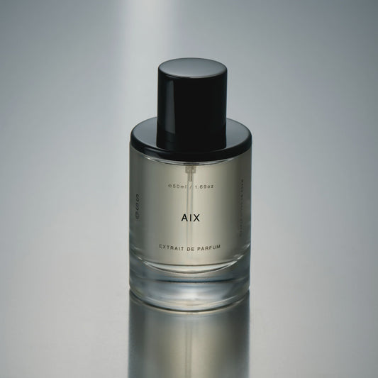 Perfume bottle labeled 'AIX' on a reflective gray surface