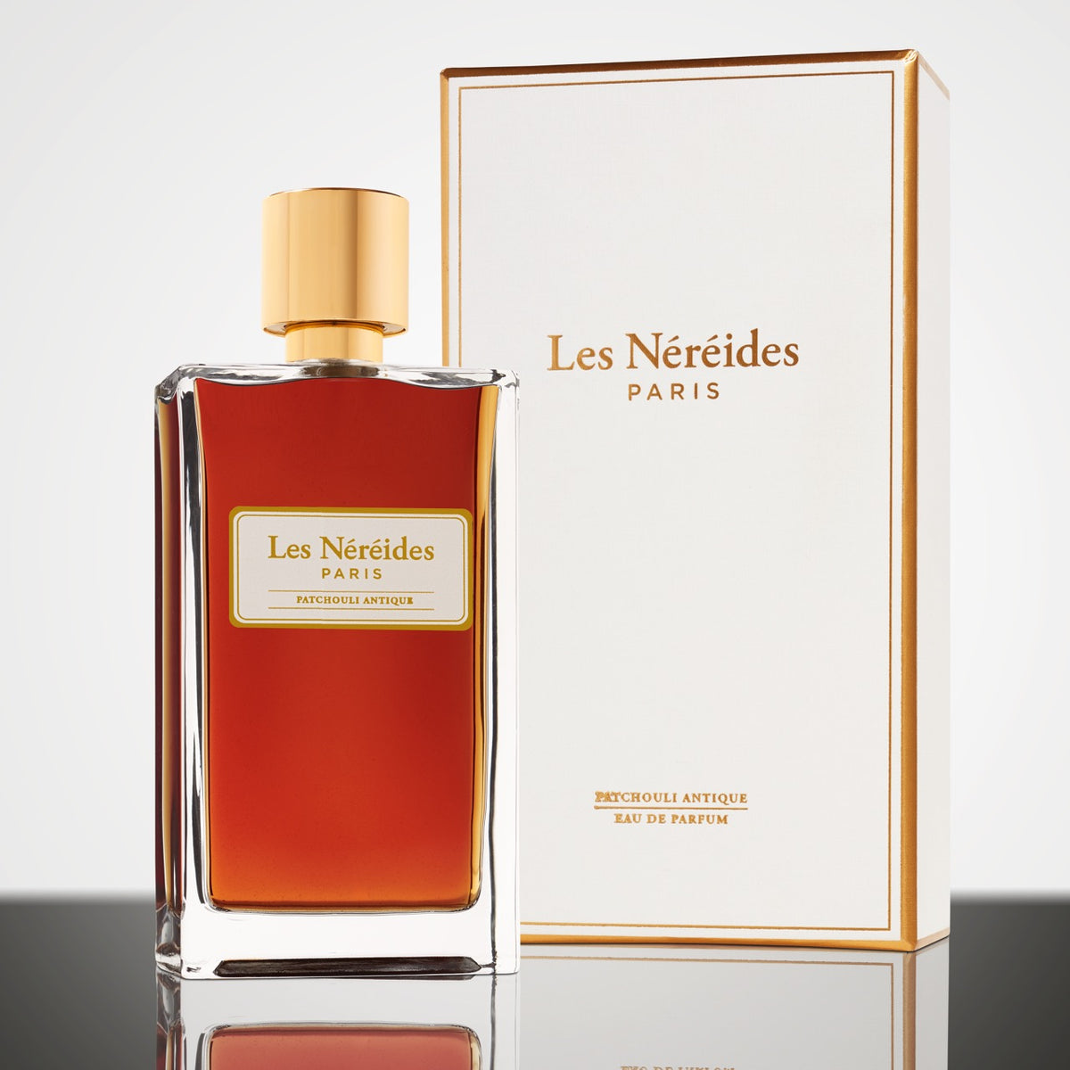Amber coloured perfume in clear bottle with gold lid, white/gold logo and white box with gold trimming